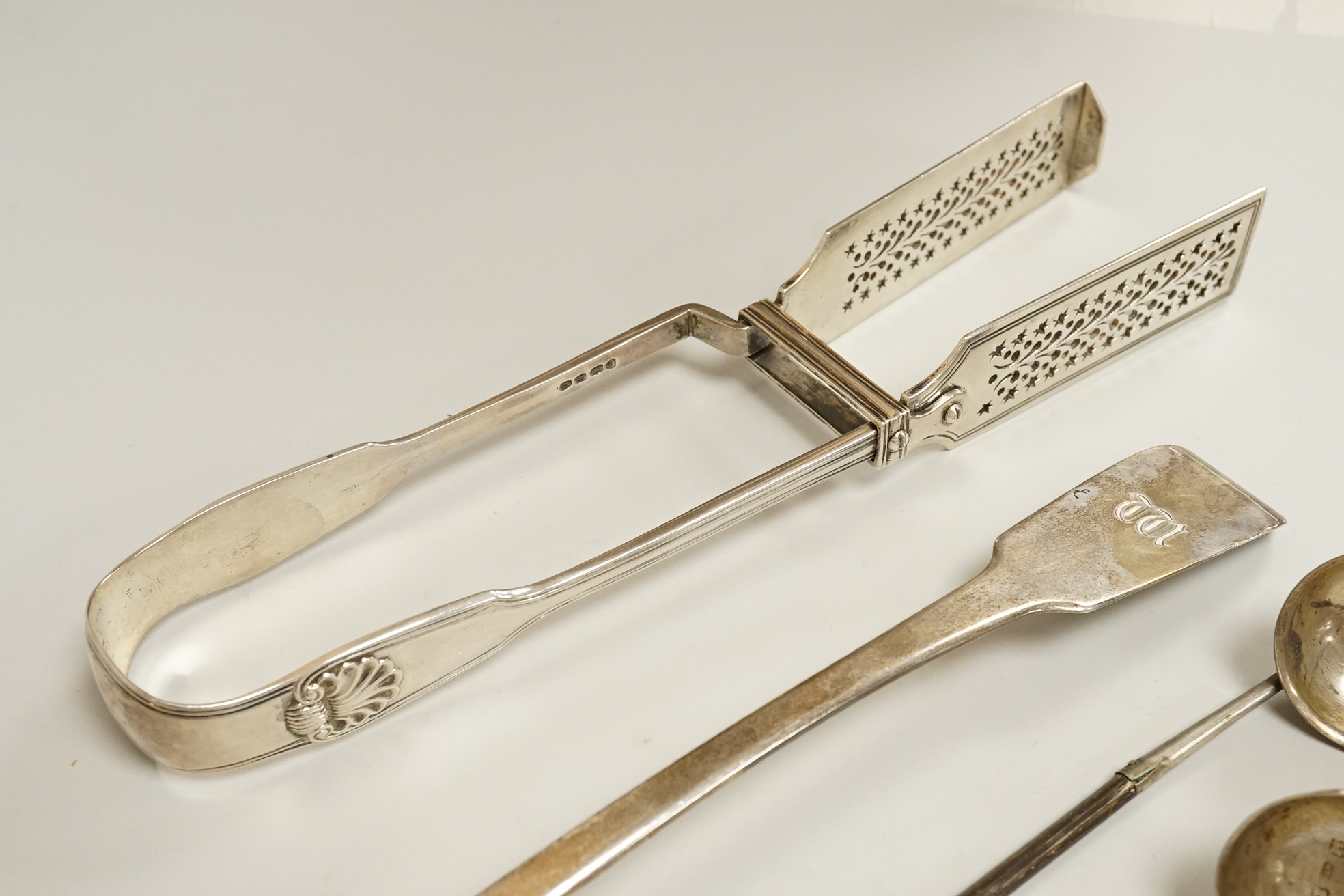 A pair of William IV silver fiddle, thread and shall pattern asparagus servers, a George IV silver fiddle pattern basting spoon, Robert Gainsford, Sheffield, 1826, 31.2cm, 10.8oz and two 19th century white metal toddy la